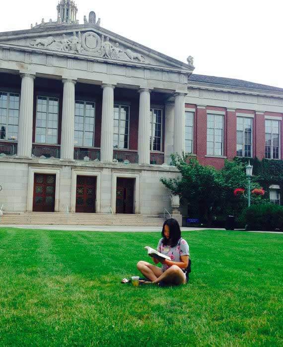 Student reading a book on college campus quad